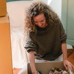 Package Deals - Happy woman unpacking carton box in living room