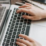 High-Speed Internet - From above of unrecognizable woman sitting at table and typing on keyboard of computer during remote work in modern workspace